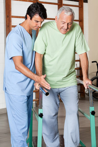 Male Physical Therapist helping assist an elderly man walk while holding on to railing with each hands.