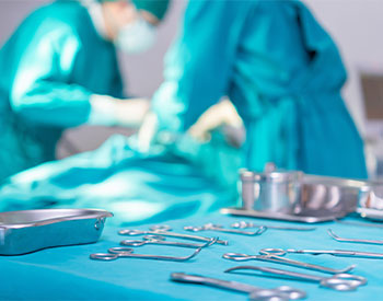 Surgical instruments and tools including scalpels, forceps, and tweezers arranged on a table for surgery, Operation room, and two Surgeons performing a Surgery on a patient.