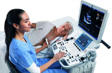 Female radiology tech administering a cardiac echo to male patient, lying on an echo table.